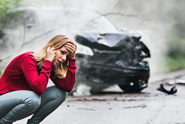 Kobieta kuca przed rozbitym samochodem i rozmawia przez telefon